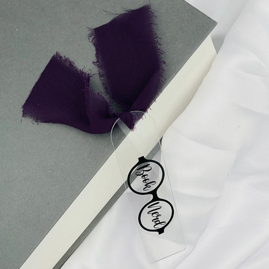 Liebevoll gestaltetes, abgerundetes Lesezeichen aus Acryl mit dunkellila Chiffonband und beklebt mit schwarzer Folie im Brillenmotiv mit "Book Nerd" in den Gläsern