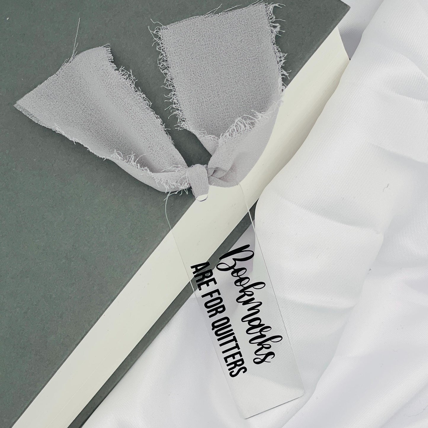 Liebevoll gestaltetes, abgerundetes Lesezeichen aus Acryl mit weißem Chiffonband und beklebt mit schwarzem Folienaufdruck "Bookmarks are for Quitters"