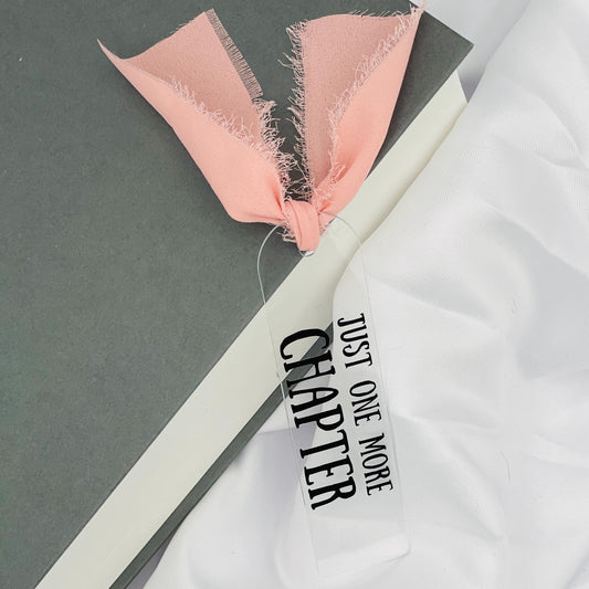 Liebevoll gestaltetes, abgerundetes Lesezeichen aus Acryl mit rosa Chiffonband und beklebt mit schwarzem Folienaufdruck "Just one more chapter"