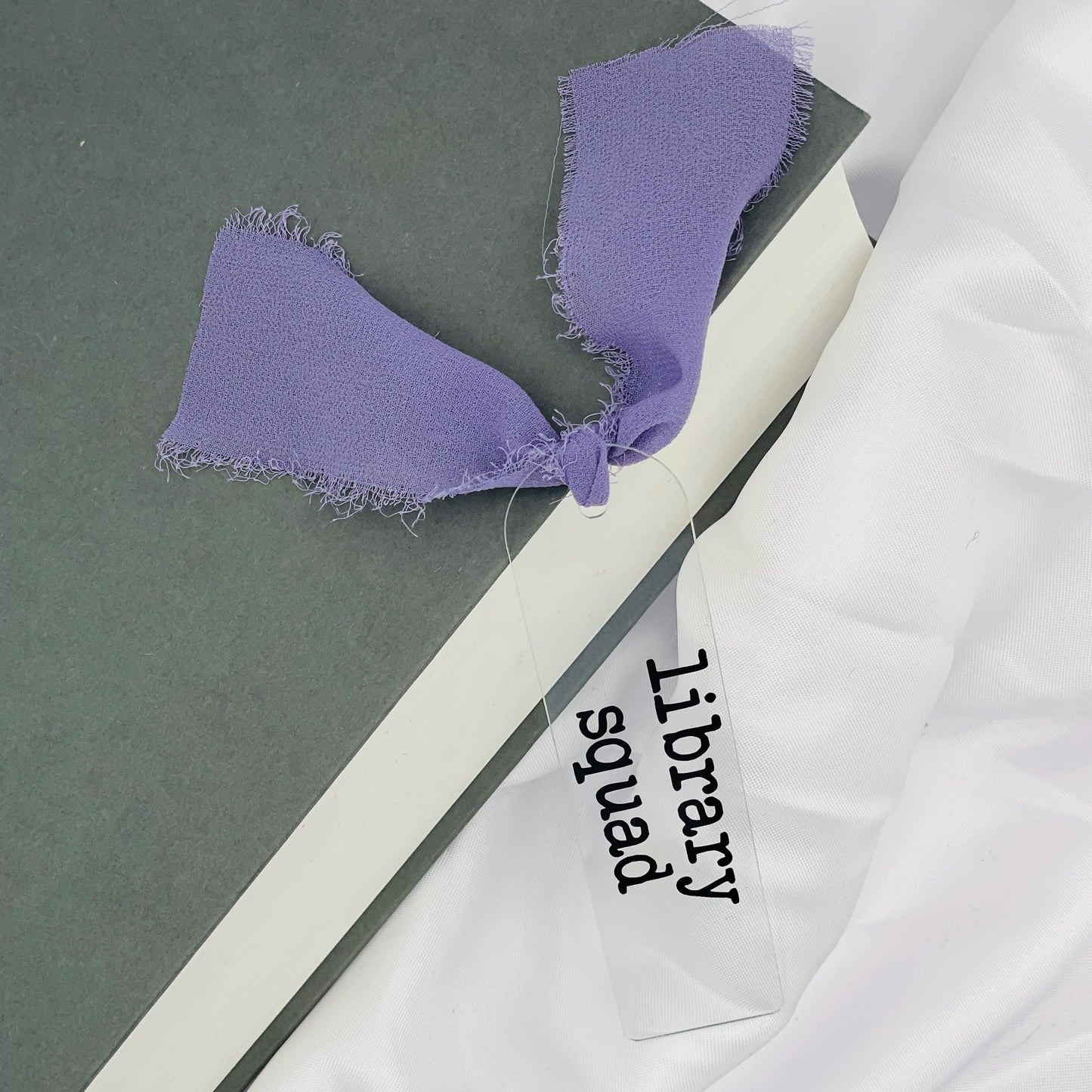 Liebevoll gestaltetes, abgerundetes Lesezeichen aus Acryl mit flieder Chiffonband und beklebt mit schwarzem Folienaufdruck "library squad"