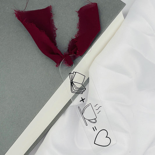 Liebevoll gestaltetes, abgerundetes Lesezeichen aus Acryl mit dunkelrotem Chiffonband und beklebt mit schwarzer Folie im Muster "geöffnetes Buch PLUS Kaffeetasse IST Herz"