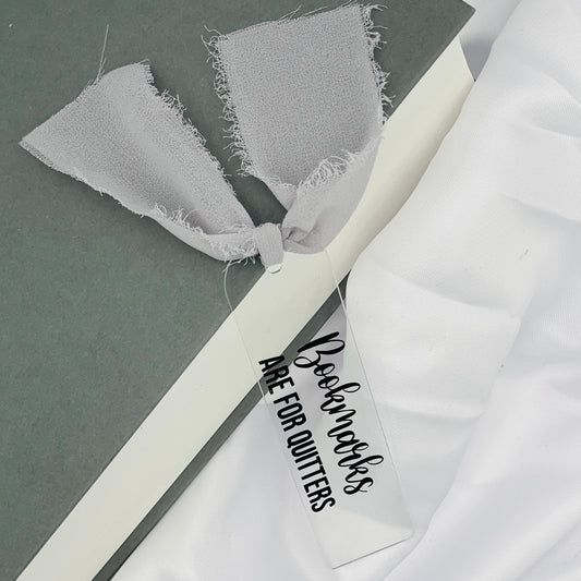 Liebevoll gestaltetes, abgerundetes Lesezeichen aus Acryl mit weißem Chiffonband und beklebt mit schwarzem Folienaufdruck "Bookmarks are for Quitters"
