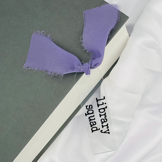 Liebevoll gestaltetes, abgerundetes Lesezeichen aus Acryl mit flieder Chiffonband und beklebt mit schwarzem Folienaufdruck "library squad"