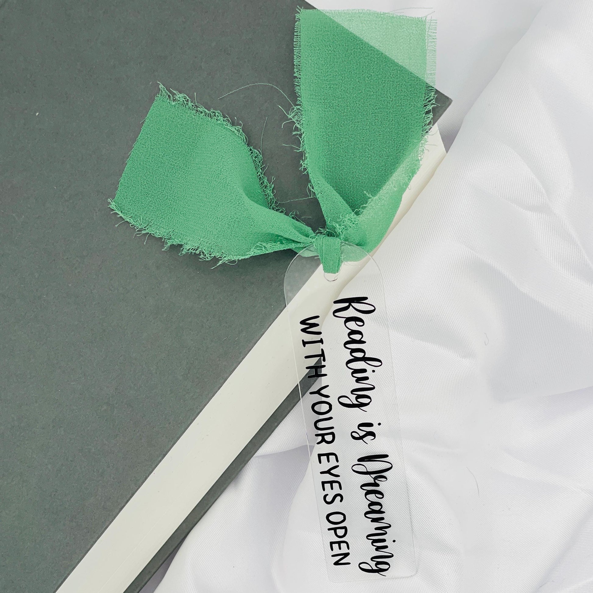 Liebevoll gestaltetes, abgerundetes Lesezeichen aus Acryl mit hellgrünem Chiffonband und beklebt mit schwarzem Folienaufdruck "Reading is Dreaming with your eyes open"