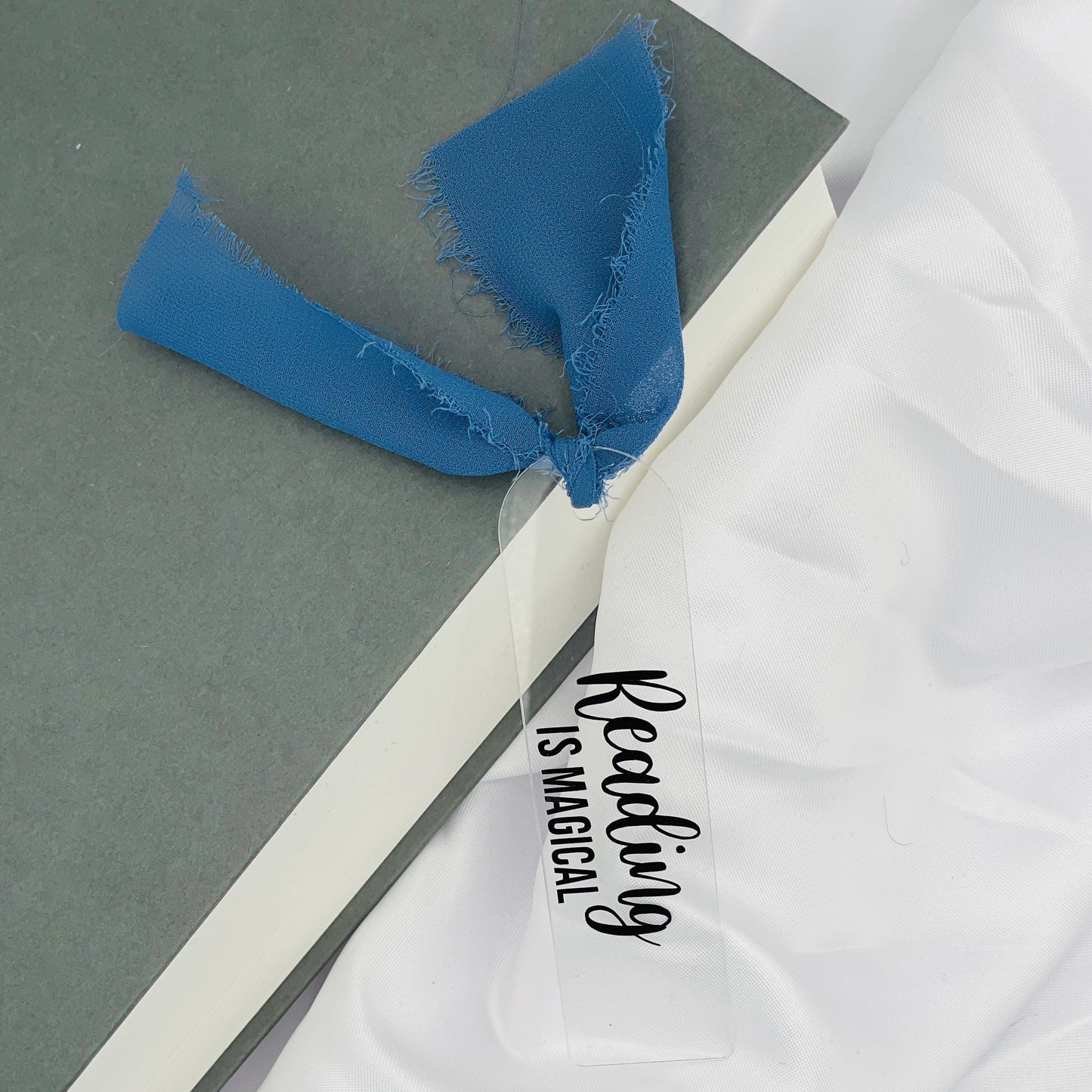 Liebevoll gestaltetes, abgerundetes Lesezeichen aus Acryl mit dunkelblauem Chiffonband und beklebt mit schwarzem Folienaufdruck "Reading is magical"