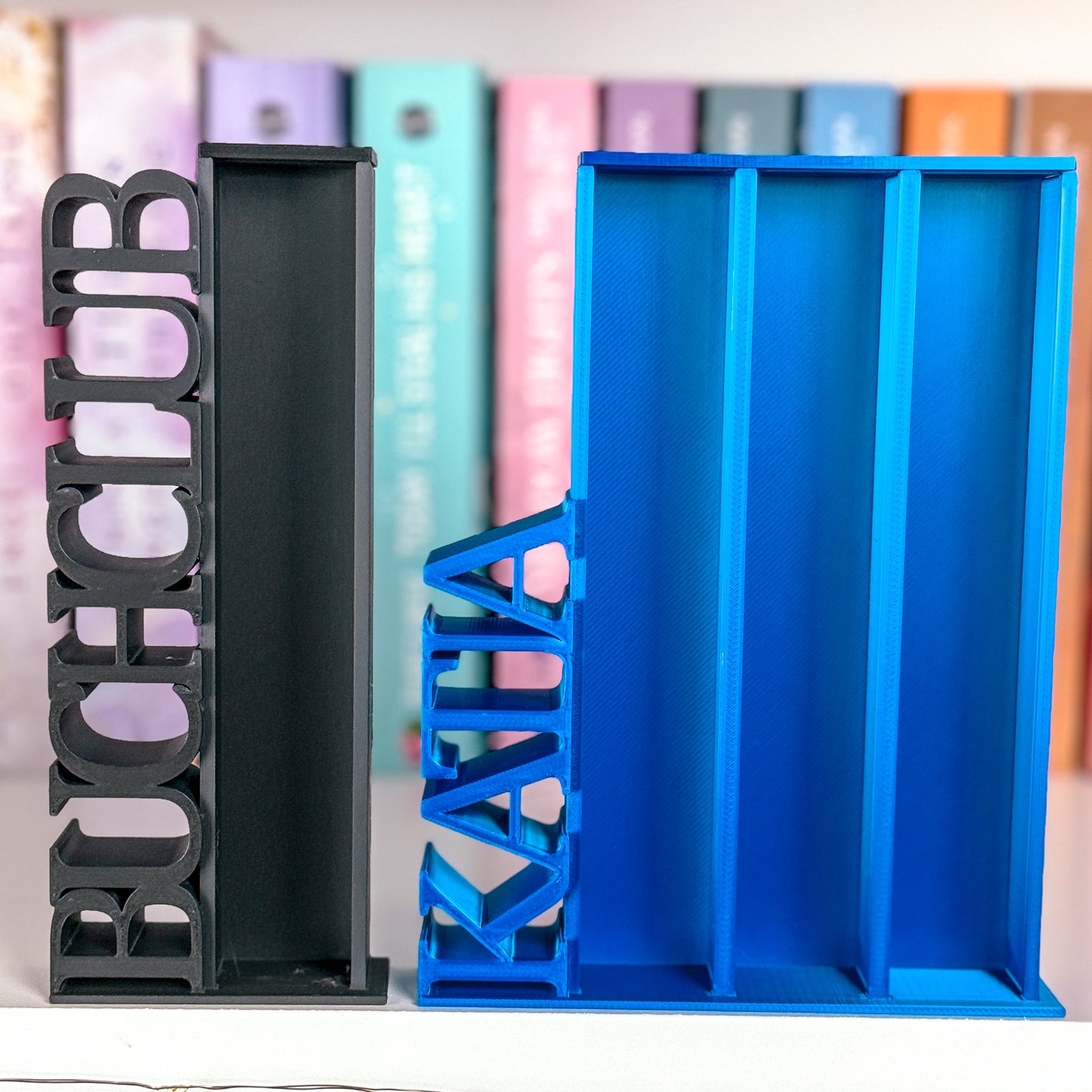 Milieuansicht 3D-gedruckter Lesezielturm im Farbton Schwarz Matt bietet Platz für 50 Mini-Bücher als Sonderanfertigung mit vertikalem "BUCHCLUB" Schriftzug und Lesezielturm im Farbton Saphir Blau bietet Platz für 150 Mini-Bücher als Sonderanfertigung mit vertikalem "KATJA" Schriftzug