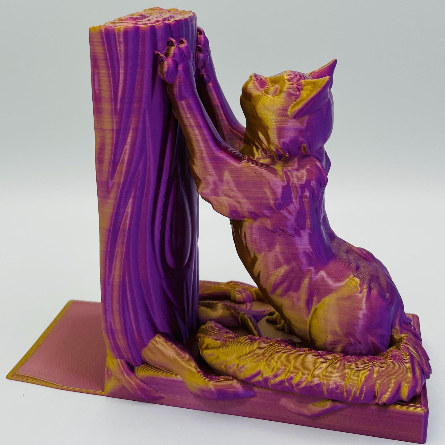 Detaillierte Ansicht einer 3D-gedruckten Buchstütze einer süßen, sitzenden Katze in Seitenansicht, die sich mit ihren Vorderpfoten an einen Baum streckt im Farbton Lila-Gold
