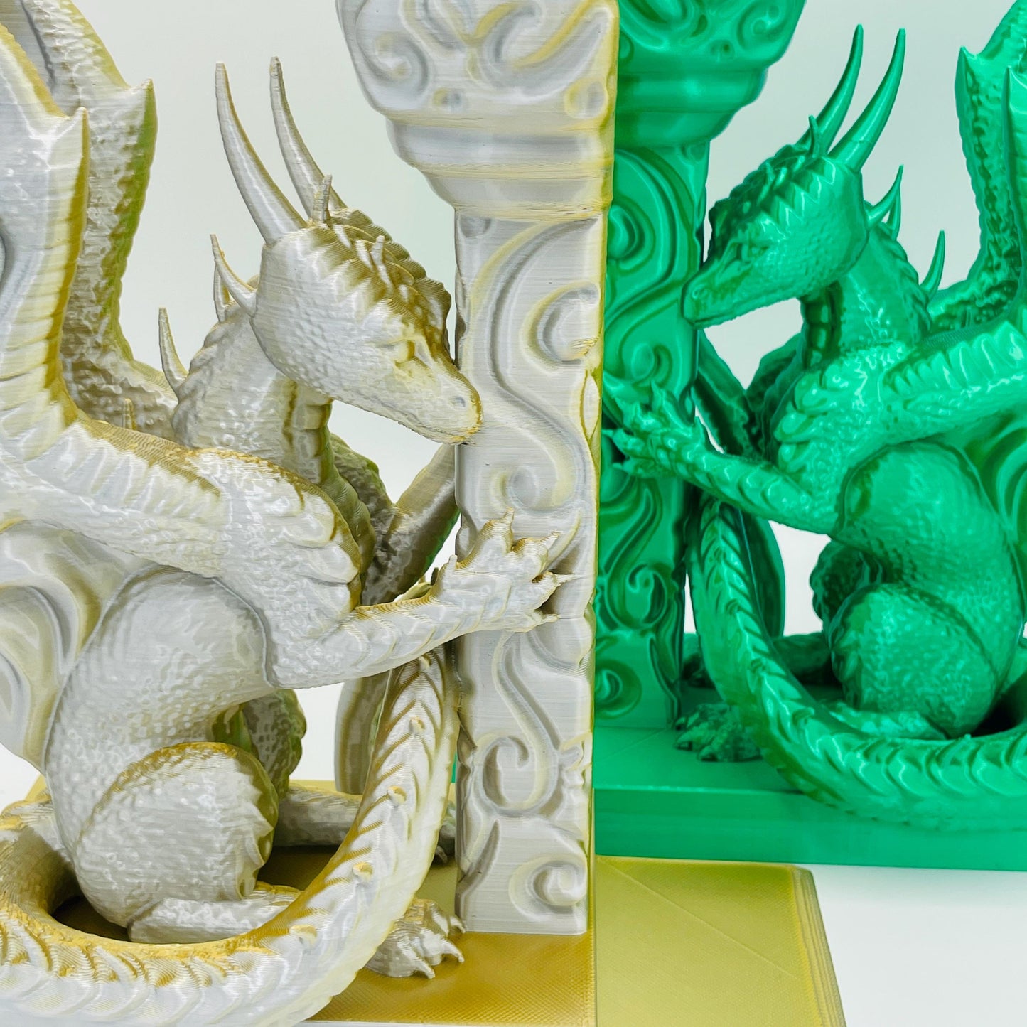 Detaillierte Ansicht der Buchstützen in Form eines Drachens in Seitenansicht, angelehnt an eine Säule in den Farbtönen Smaragd Grün und Gold-Silber im Direktvergleich