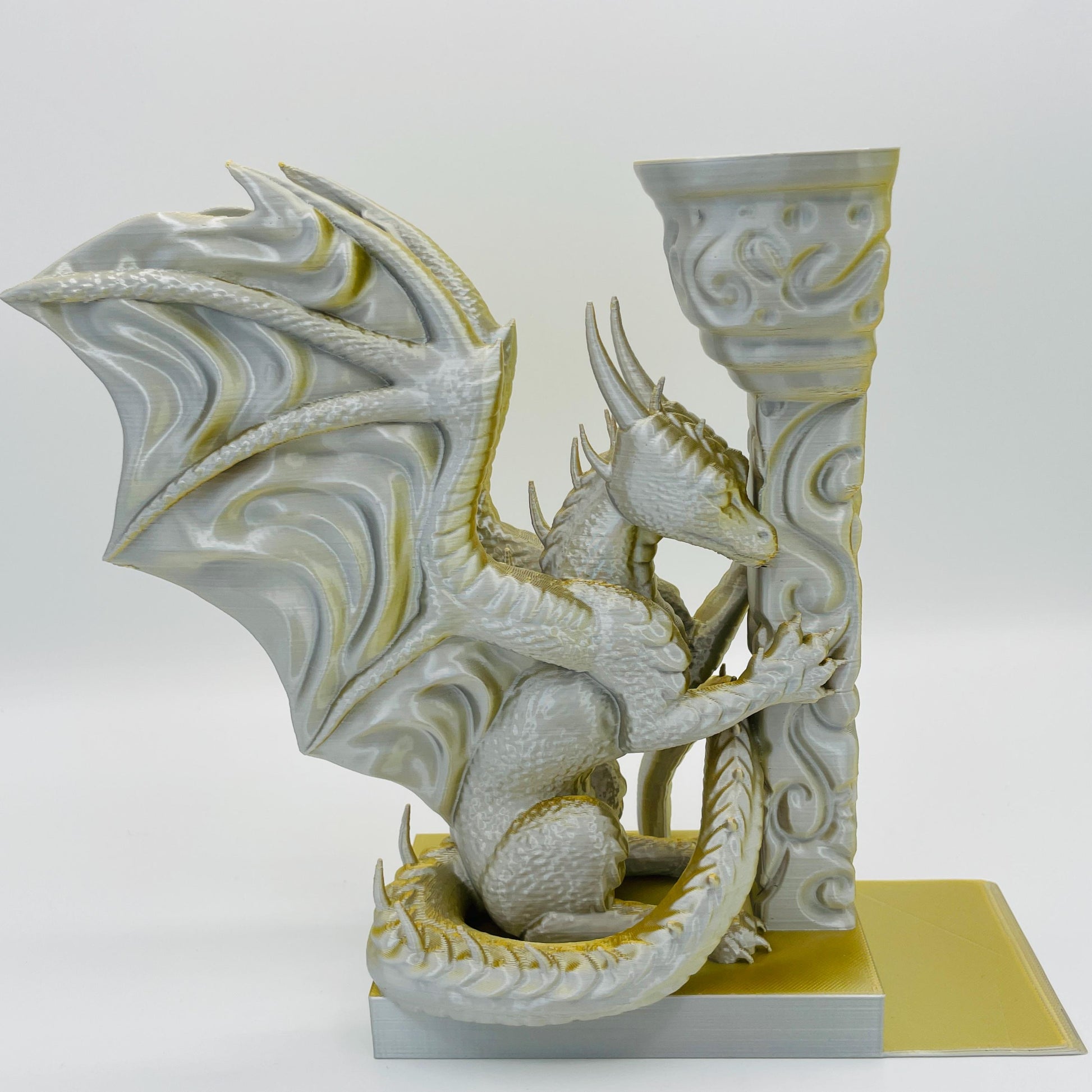 Detailliertere Ansicht einer 3D-gedruckten Buchstütze eines Drachens in Seitenansicht, angelehnt an eine Säule im Farbton Gold-Silber