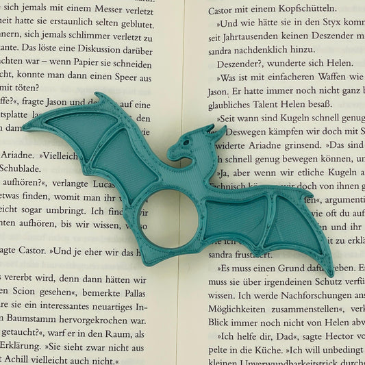 Frontansicht eines 3D-gedruckten Buchseitenhalters in Form eines Drachen mit Lochaussparung für Finger im Farbton Metallic Türkis