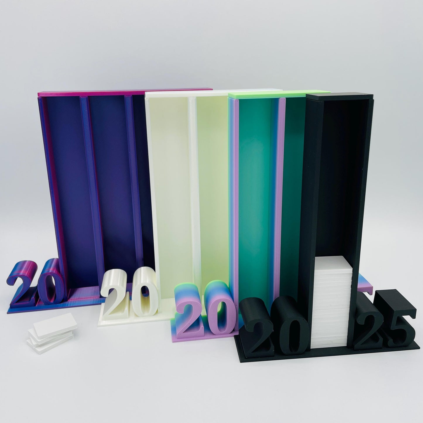Frontansicht 3D-gedruckte Lesetürme mit 2025 Schrift im Vergleich, 4 Spalten in Blau-Pink-Lila, 3 Spalten in Perlmutt Weiß, 2 Spalten in RB Matt Regenbogen-Farbverlauf und 1 Spalte in Matt Schwarz für je 50 Mini-Bücher