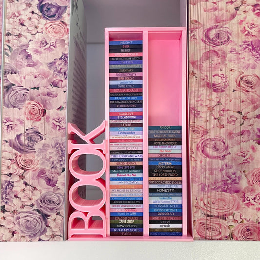 Milieuansicht 3D-gedruckter Lesezielturm im Farbton Rosa bietet Platz für 100 Mini-Bücher mit vertikalem "BOOK" Schriftzug, zwischen zwei Büchern mit Blumenfarbschnitt
