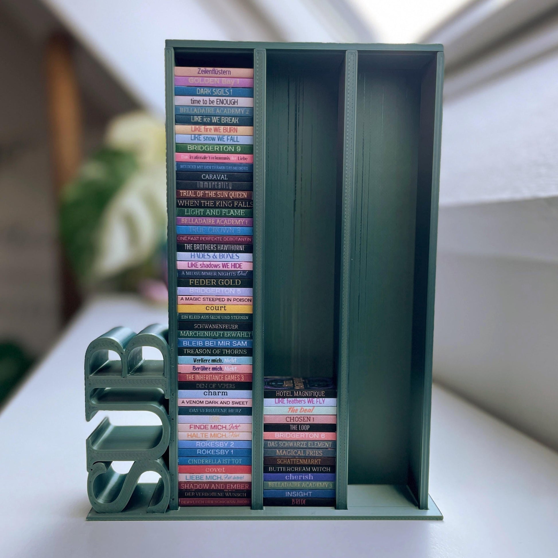 Milieuansicht 3D-gedruckter Lesezielturm im Farbton Olive bietet Platz für 150 Mini-Bücher mit vertikalem "SUB" Schriftzug, auf einem Bücherregal