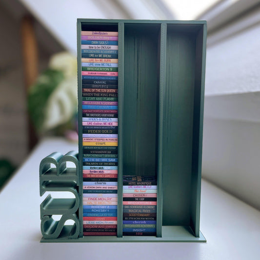 Milieuansicht 3D-gedruckter Lesezielturm im Farbton Olive bietet Platz für 150 Mini-Bücher mit vertikalem "SUB" Schriftzug, auf einem Bücherregal