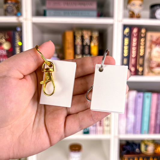 Milieuansicht zwei Schlüsselanhänger "Minibuch" links mit goldenem Schlüsselring und Karabiner, rechts mit silbernem Schlüsselring und Karabiner
