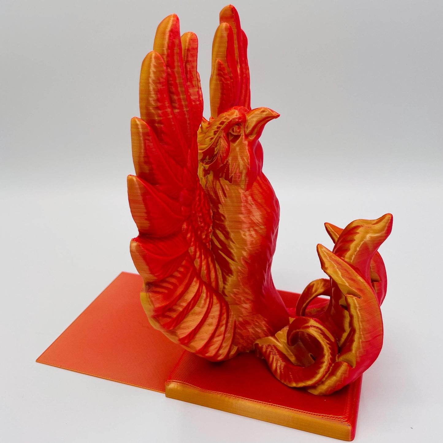 Detaillierte, diagonale Ansicht einer 3D-gedruckten Buchstütze des Oberkörpers eines stolzen Phönix mit gestreckten Flügeln im Farbton Rot-Gold