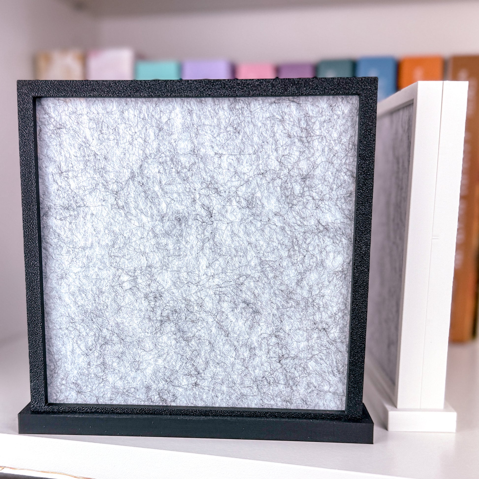 Rückseite von zwei Pin Aufstellern 3D gedruckt aus PLA. Einer in Matt Weiß und der andere in Matt schwarz. Im Inneren des Rahmens befindet sich eine graue Filz Pinwand.