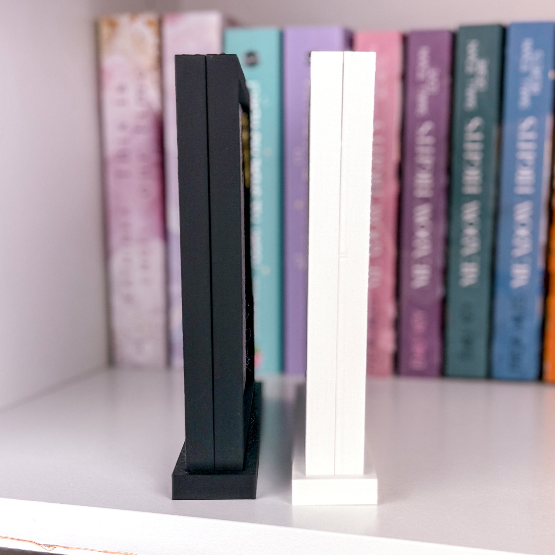 Seitenansicht von zwei Pin Aufstellern 3D gedruckt aus PLA. Einer in Matt Weiß und der andere in Matt schwarz. Im Inneren des Rahmens befindet sich eine graue Filz Pinwand. Am unteren Ende des Aufsteller ist ein breiterer Fuß mit dem der Rahmen von selber steht.