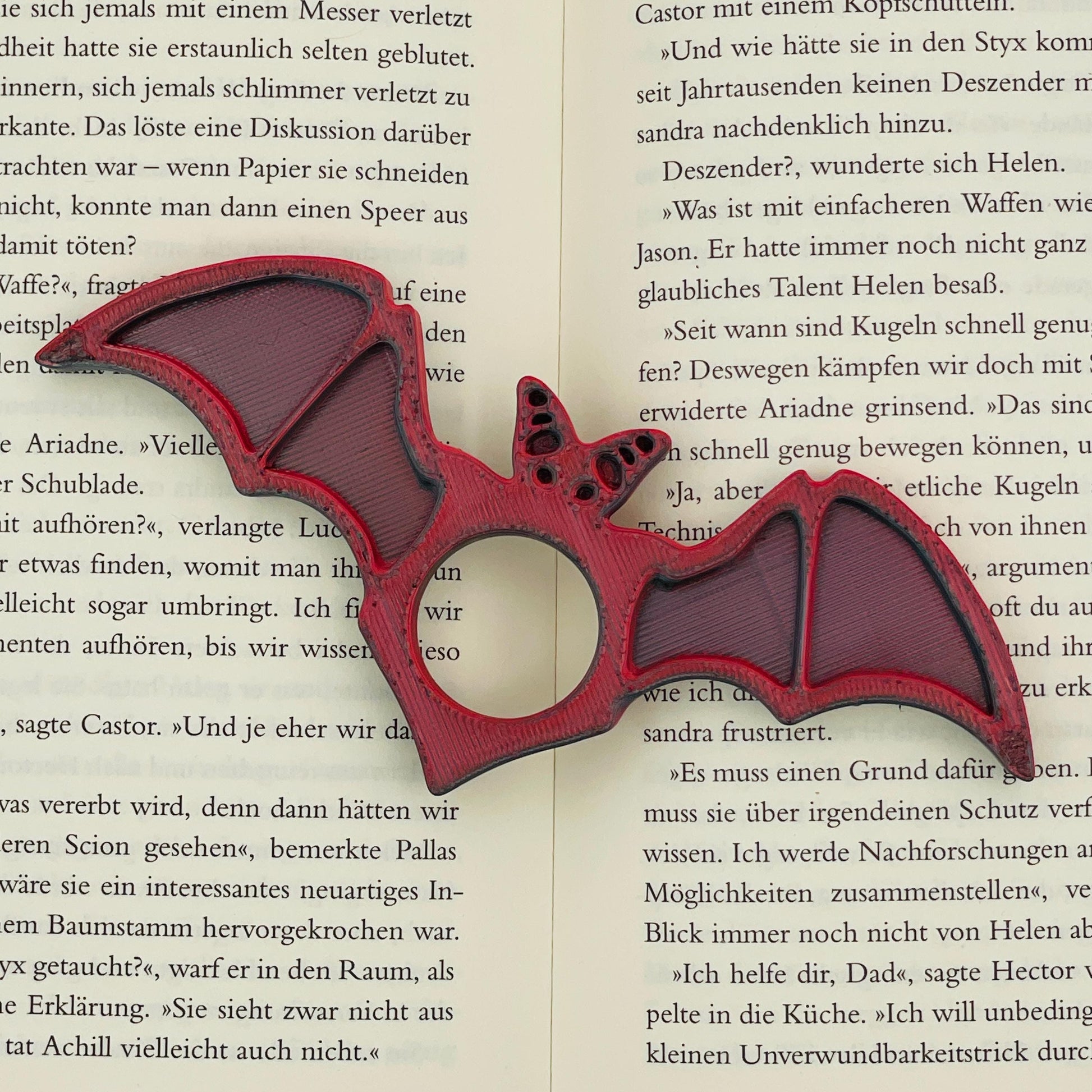 Frontansicht eines 3D-gedruckten Buchseitenhalters in Form einer Fledermaus mit Lochaussparung für Finger im Farbton Rot-Schwarz