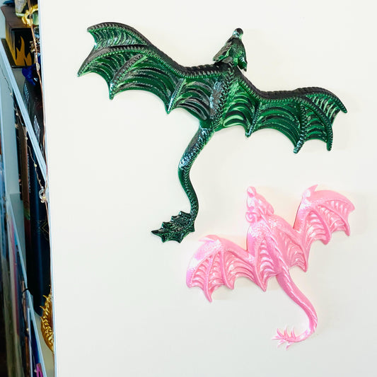 Frontansicht 3D-gedruckte Drachen mit Ansicht von Oben zur Befestigung an Wänden, einer mit gespreizten Flügeln in Grün-Schwarz und einer mit eingeklappten Flügeln in Rosa